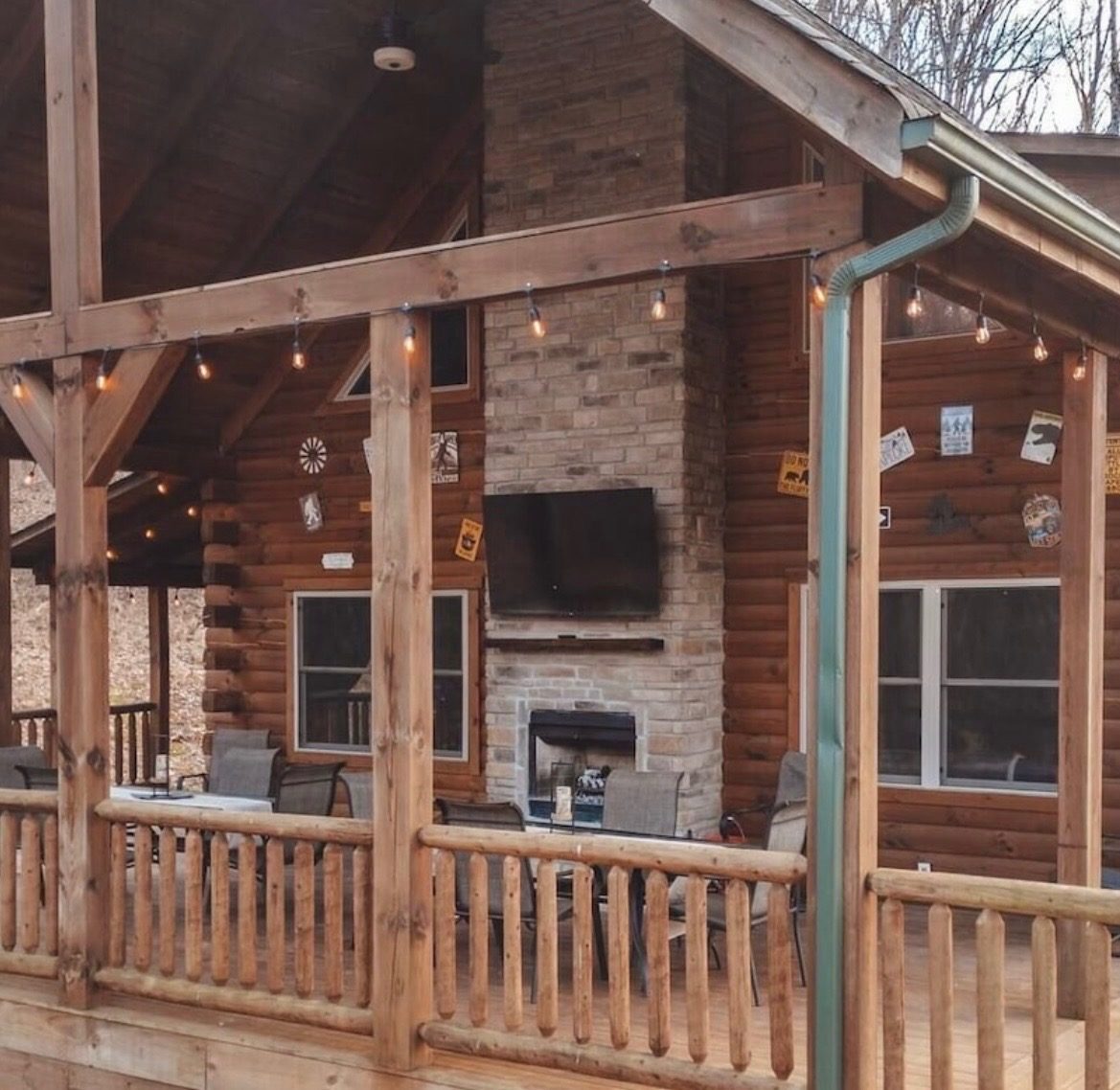 Covered deck with an outdoor stone wood-burning fireplace, TV and string lights