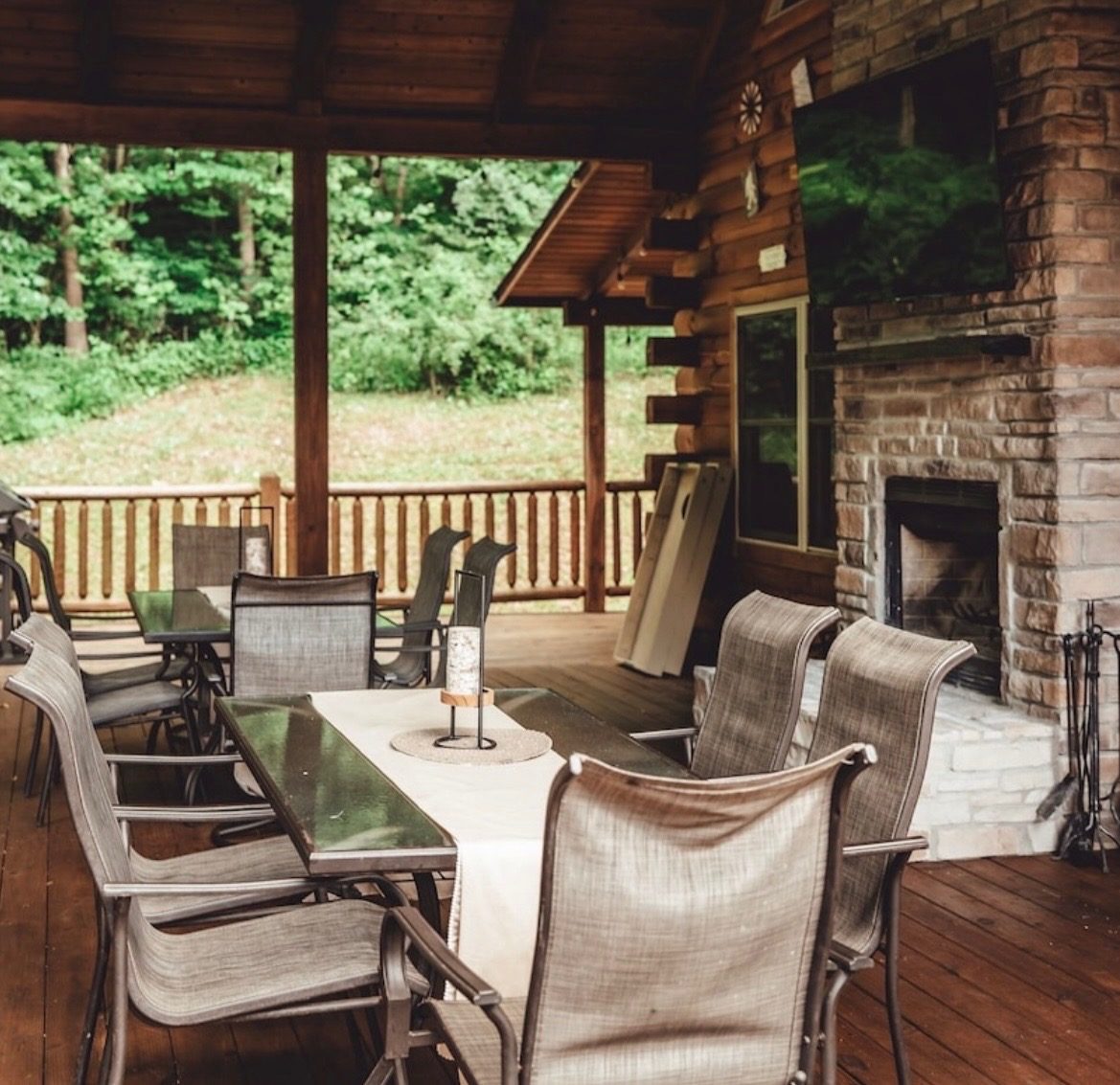 Covered deck dining tables beside the outdoor stone fireplace and TV