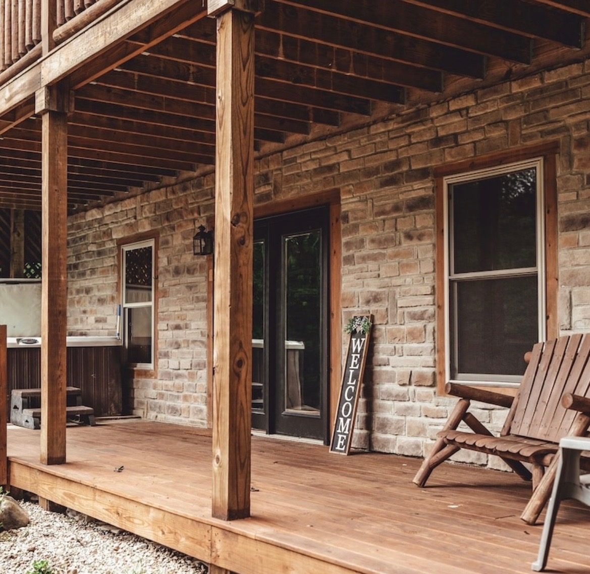 Lower covered patio with stone walls, a welcome sign and log bench