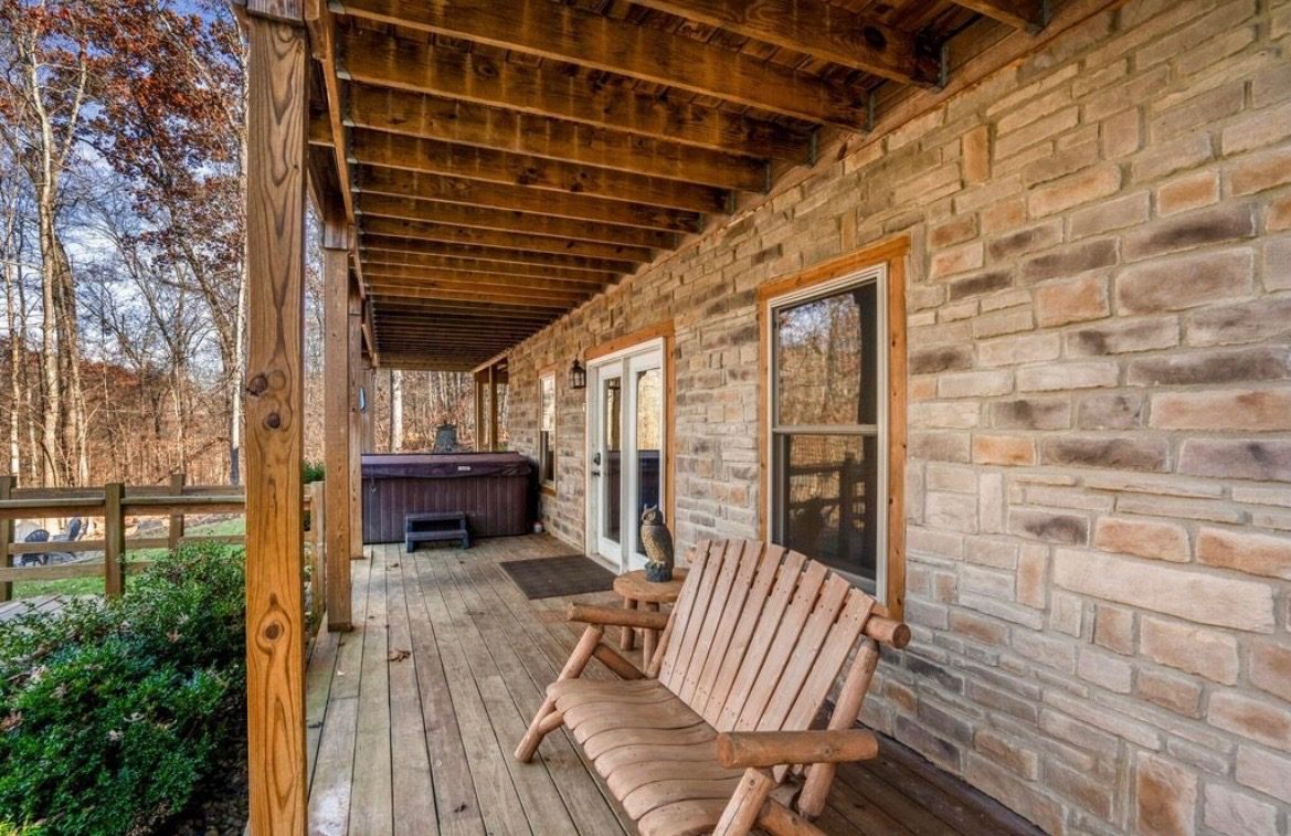 Lower covered patio with stone walls, the hot tub and a log bench