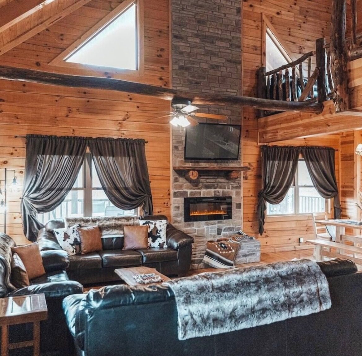 Great room with leather sofas, a stone electric fireplace with TV and a view up to the loft