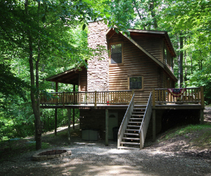 cabin side view on hill with tall stone exterior fireplace and wrap around deck